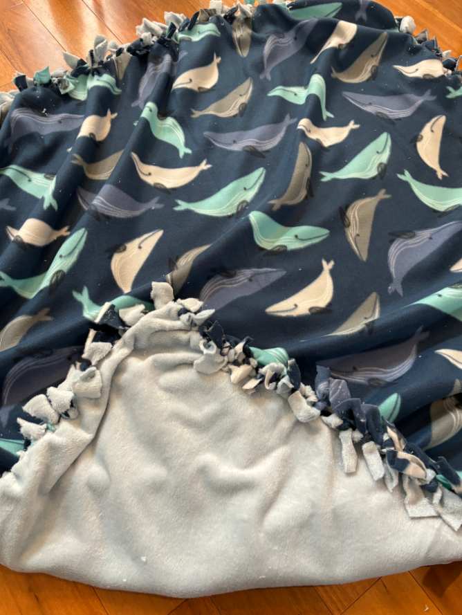 A finished DIY no-sew blanket in fleece fabric with blue whales on it, in a a close up photo.